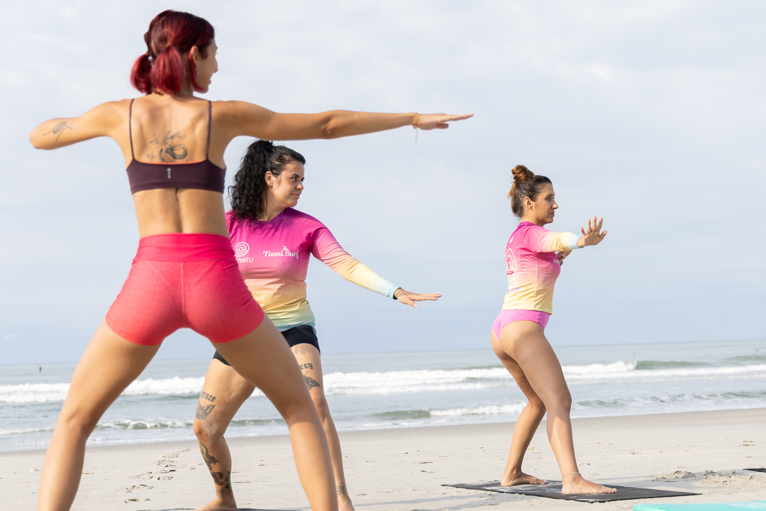 Mulheres fazendo uma prática de movimento na areia antes do surf