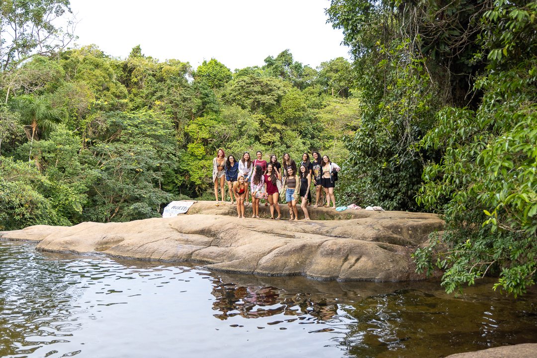 Grupo da We Surf Girls reunido em uma cachoeira cercada de mata